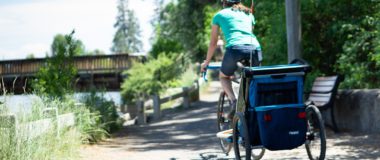woman biking with kid trailer on trail